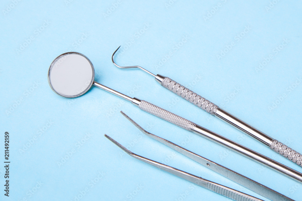 Dental instruments. Dental mirror, probe hook, tweezers on blue Dental instruments. Dental mirror, probe hook, tweezers on blue