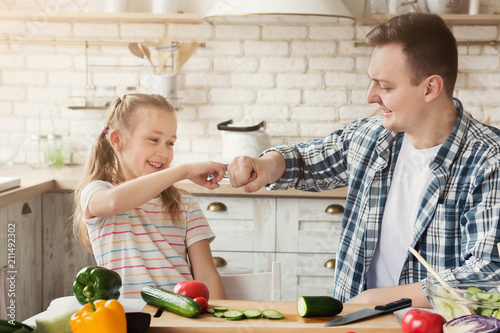 Cute little girl and her father bumping fists at kitchen