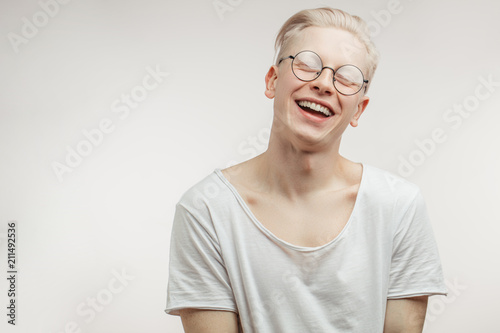 Happy blonde man in spactacles with uncommon handsome appearance smiling into camera having pleased dreaming expression being happy with coming holidays.