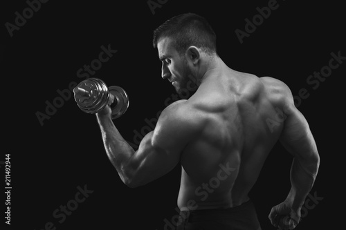 Strong man with dumbbell showing muscular body © Prostock-studio