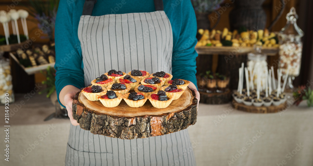 Chef holding wooden tray with berry tartlets
