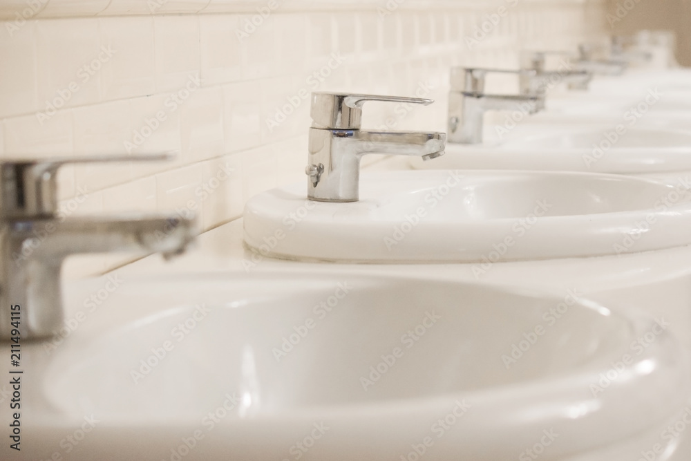Many Closed chrome-plated faucets stand in a row in a public toilet. The room is clean and bright. Many Closed chrome-plated faucets stand in a row in a public toilet. The room is clean and bright.