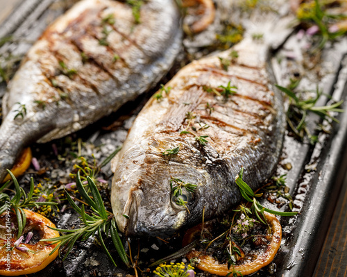 Grilled fish with herbs and lemon on a grill plate, close up view. Grilled sea bream, barbecue photo