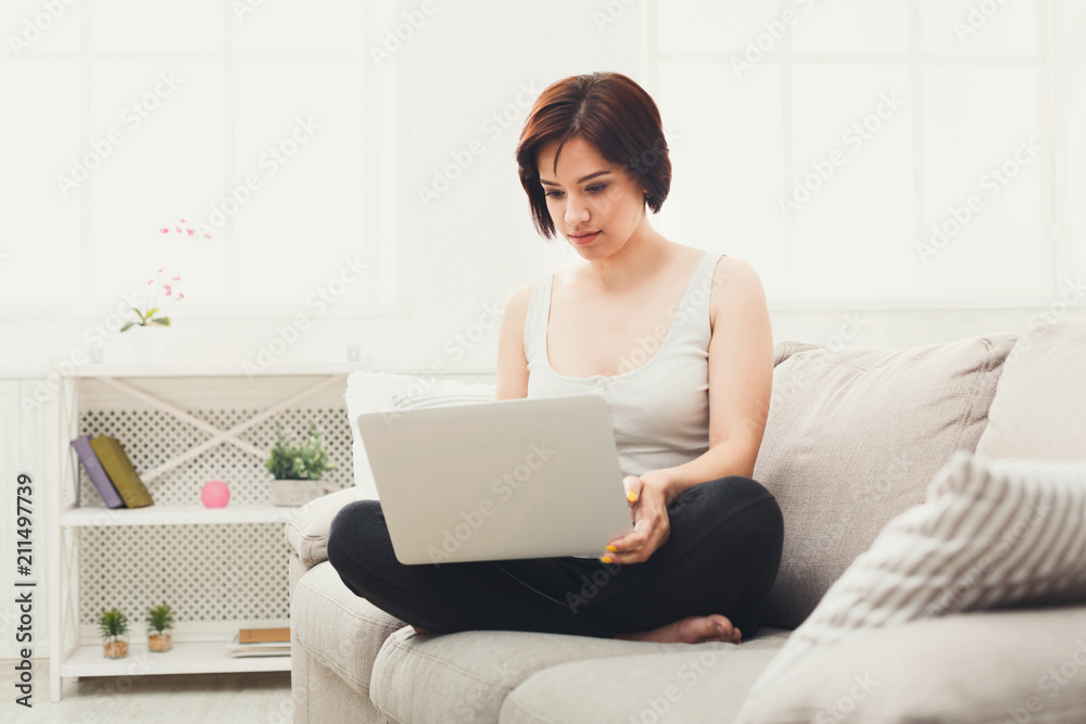 Young brunette girl with laptop sitting on beige couch Young brunette girl with laptop sitting on beige couch