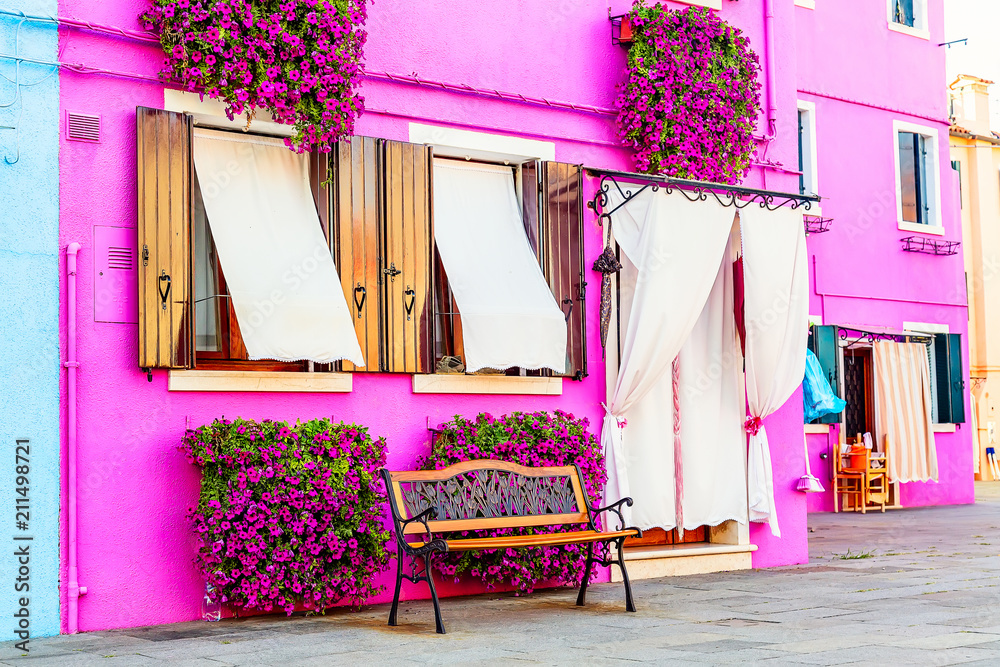 Obraz premium Różowy dom z różowymi kwiatami i roślinami. Ładna ławka pod oknami. Kolorowy dom na wyspie Burano w pobliżu Wenecji, Włochy