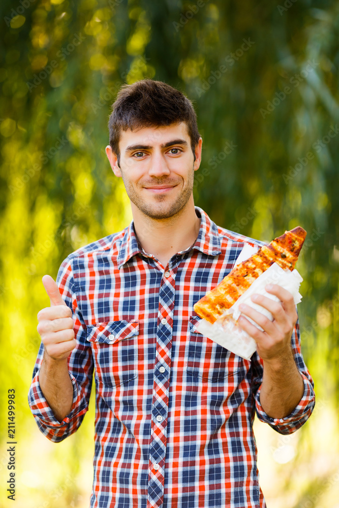 Fototapeta premium Cheerful young guy is eating pizza on the park