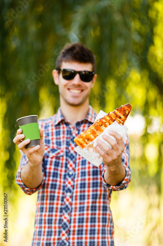 Man eating pizza. Cheerful young guy is eating pizza drinking coffee on the park © Parfenova