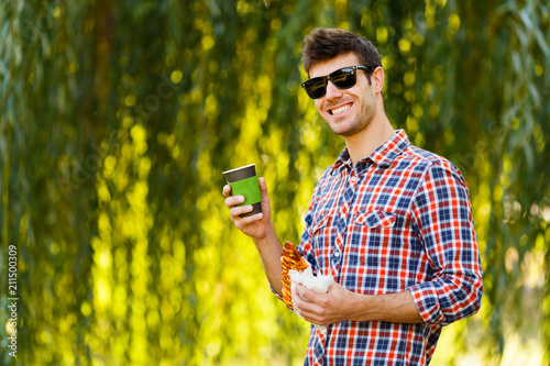 Man eating pizza. Cheerful young guy is eating pizza drinking coffee on the park photo