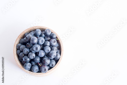 Fresh forest blueberries in a wooden cup on a white background closeup, top view.