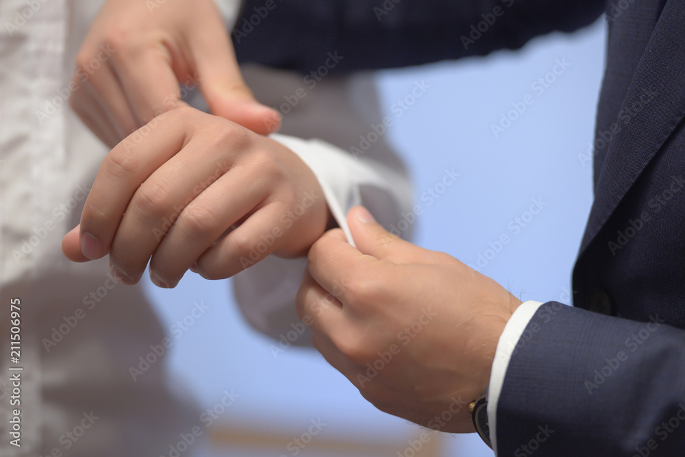 Obraz premium Close-up shot of hands of young white Caucasian male being helped with his white shirt by another elegantly dressed man. Classy groom, stylish businessman, or millennial male model getting ready.