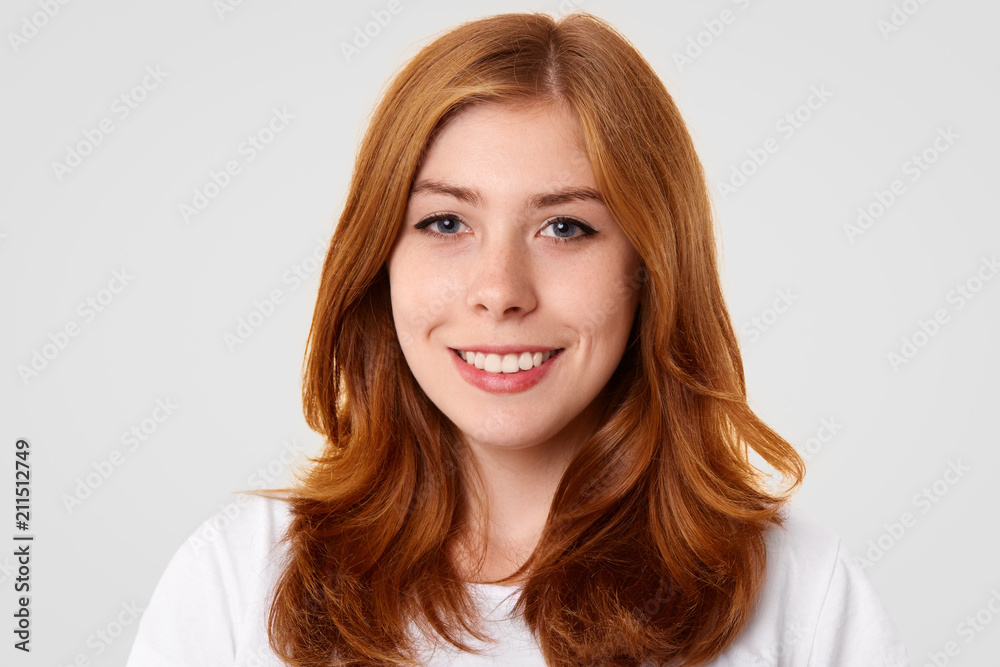 Close up portrait of pretty freckled female with dyed hair, has friendly smile, rejoices weekend, going to spend free time with friends against white background. People and positive emotions