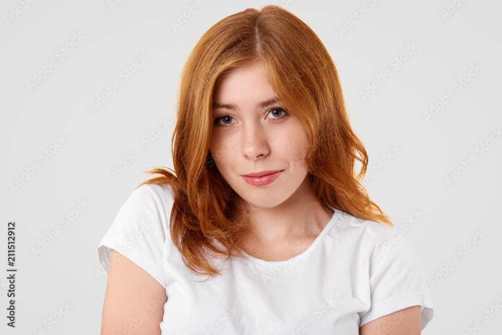 Adorable cute young female with shy expression, has mysterious look and dyed bushy hair, dressed in casual white t shirt, isolated over studio background. People, beauty and lifestyle concept Adorable cute young female with shy expression, has mysterious look and dyed bushy hair, dressed in casual white t shirt, isolated over studio background. People, beauty and lifestyle concept