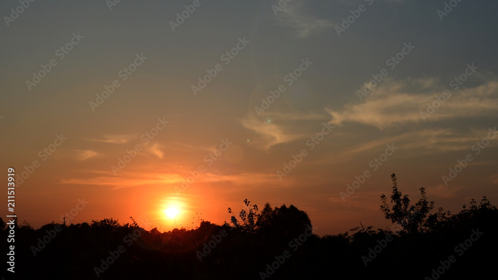 Rays of sunset through dark clouds with a contour of trees on the horizon.