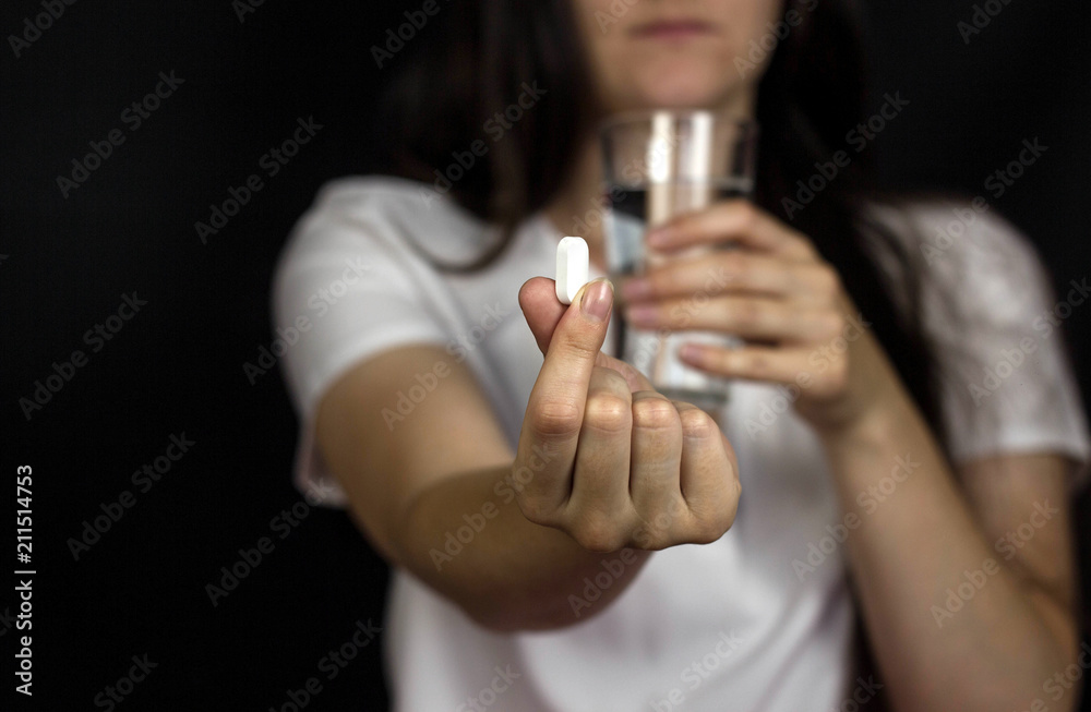 Young girl holding a pill in her hand and a glass of water, close-up Young girl holding a pill in her hand and a glass of water, close-up