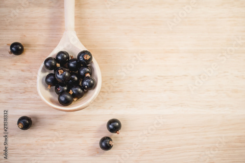 A black currant in a wooden spoon on a table.
