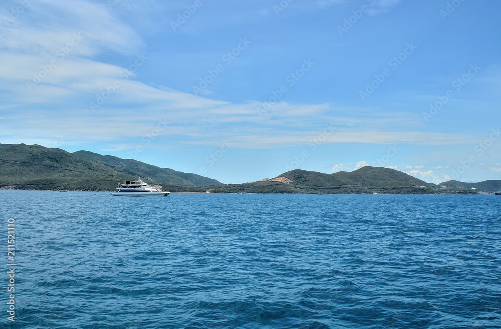 white walking catamaran in the sea, near the coastline of the island, against a background of sushi covered with greenery, the sky is covered with clouds white walking catamaran in the sea, near the coastline of the island, against a background of sushi covered with greenery, the sky is covered with clouds
