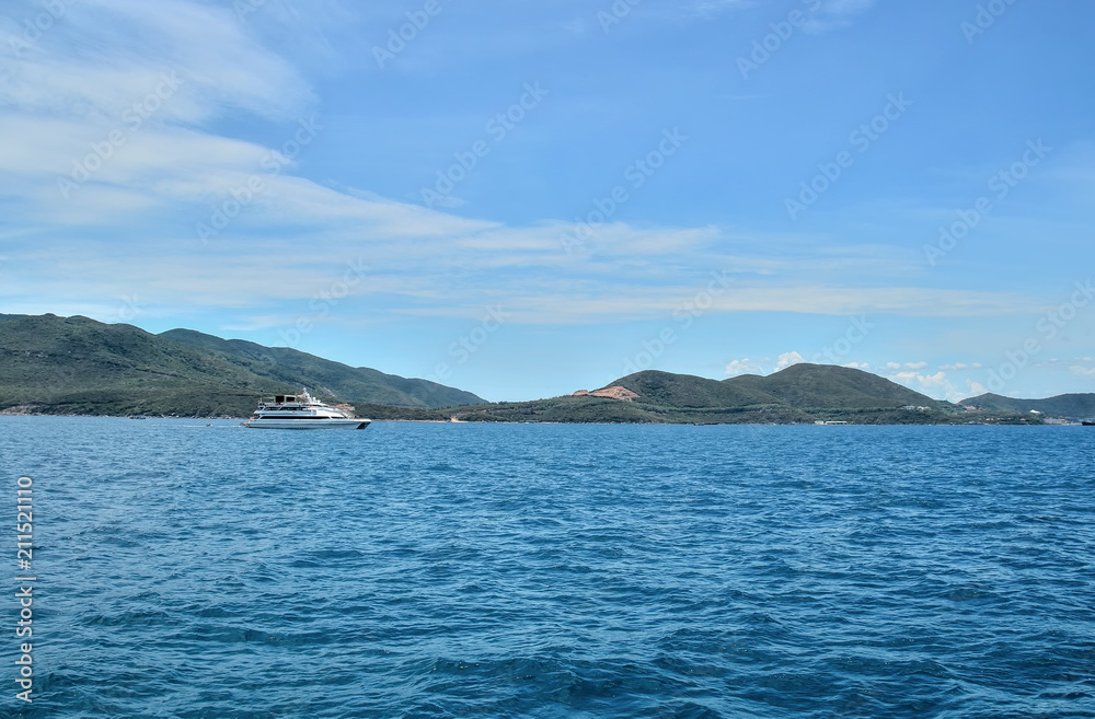 white walking catamaran in the sea, near the coastline of the island, against a background of sushi covered with greenery, the sky is covered with clouds