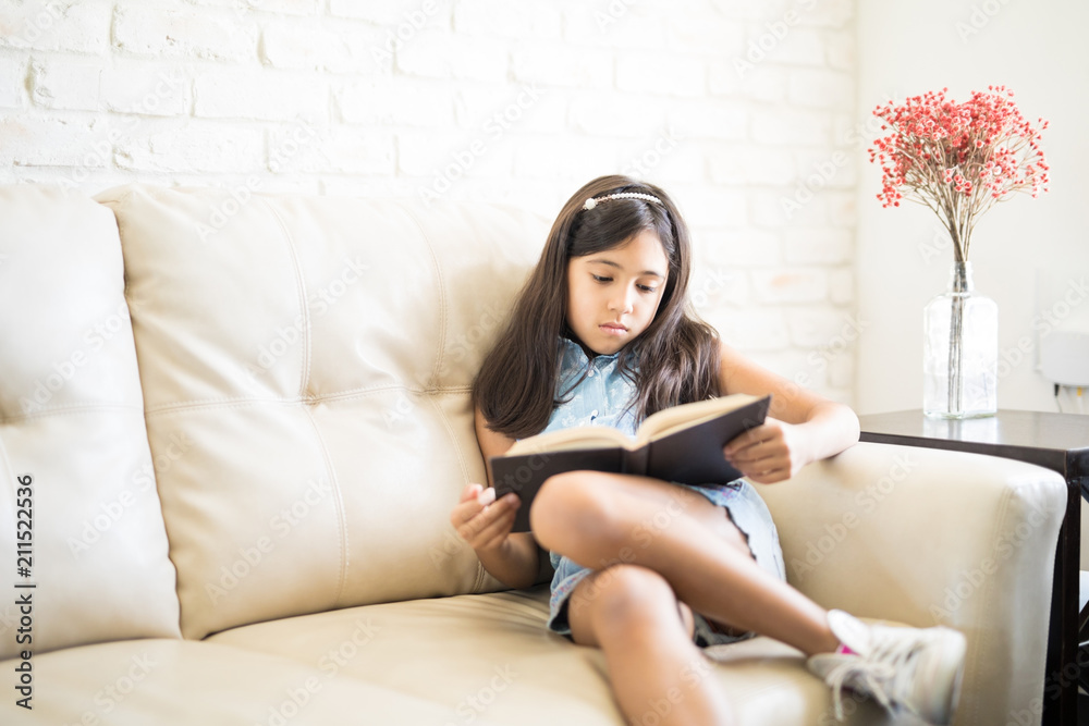 Portrait of 9 years old girl reading a book sitting on couch at home Portrait of 9 years old girl reading a book sitting on couch at home