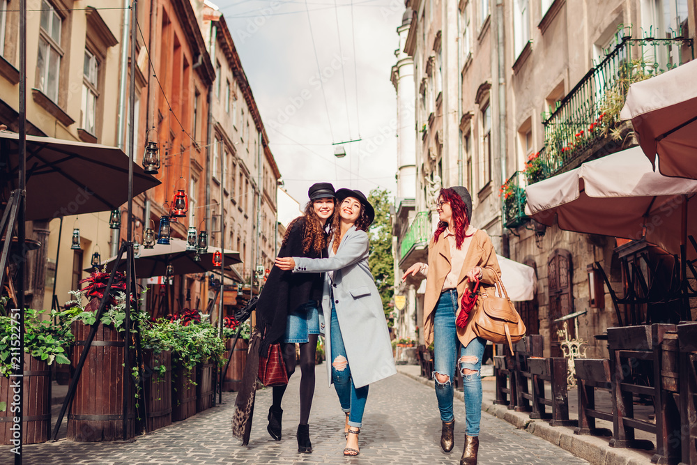 Outdoor shot of three young women walking on city street. Girls talking and hugging