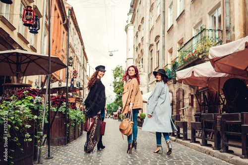 Outdoor shot of three young women walking on city street. Girls turning and looking at camera