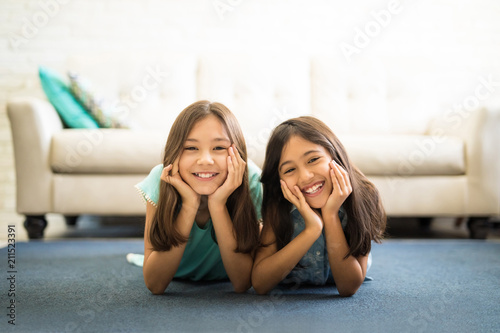Portrait of two sisters lying on the floor in living room smiling photo