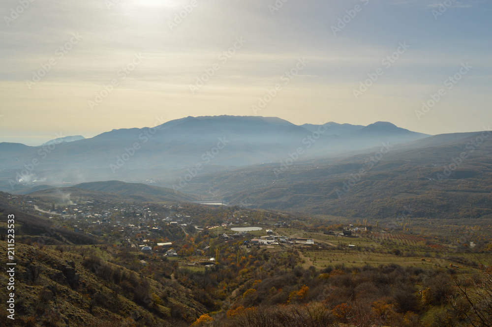 soft rays of the midday sun illuminate the autumn valley. a small village surrounded by mountains.