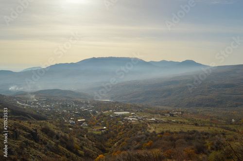 Fototapeta Naklejka Na Ścianę i Meble -  soft rays of the midday sun illuminate the autumn valley. a small village surrounded by mountains.