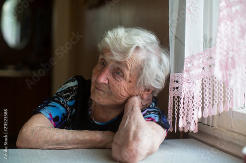 An elderly woman sits thoughtfully at the table.