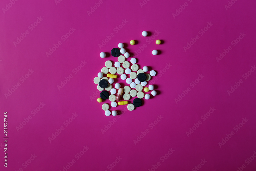 Assorted pharmaceutical medicine pills, tablets and capsules on pink background