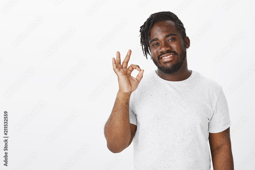 Indoor shot of satisfied happy dark-skinned customer in white t-shirt, smiling broadly with pleased expression, raising hand in okay or great gesture, liking new product and giving positive feedback Indoor shot of satisfied happy dark-skinned customer in white t-shirt, smiling broadly with pleased expression, raising hand in okay or great gesture, liking new product and giving positive feedback