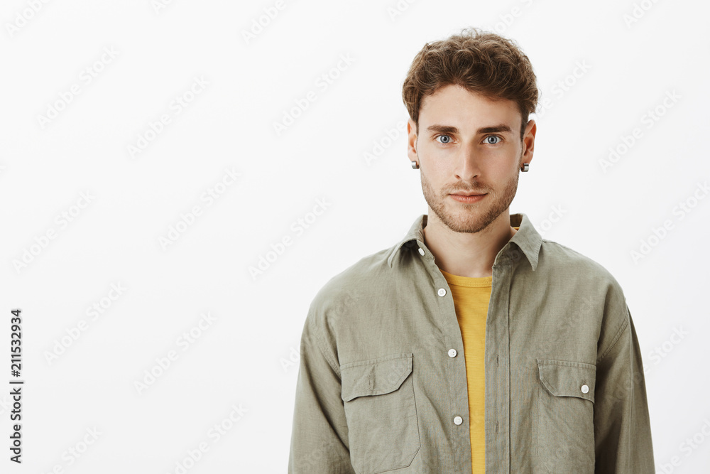 Portrait of charming bearded male coworker with earrigs and beard, smiling joyfully at camera, standing relaxed and confident over gray background, talking with friends while hanging out on festival Portrait of charming bearded male coworker with earrigs and beard, smiling joyfully at camera, standing relaxed and confident over gray background, talking with friends while hanging out on festival