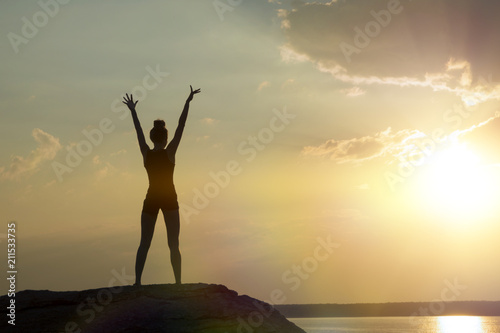 girl at the top of the mountain, raising her hands up against the sunset. Concept of sport, yoga, relaxation, meditation.