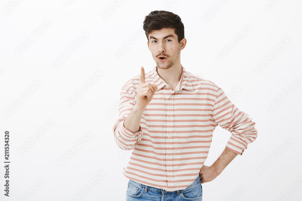 Indoor shot of suspicious playful european guy with funny expression, raising hand and shaking index finger, threatening or giving own opinion, teaching brother how to behave over gray wall Indoor shot of suspicious playful european guy with funny expression, raising hand and shaking index finger, threatening or giving own opinion, teaching brother how to behave over gray wall