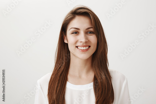 Girl is happy receive good feedback about her site. Portrait of attractive caucasian woman in white shirt smiling broadly, looking with satisfied expression at camera, feeling great after day in spa