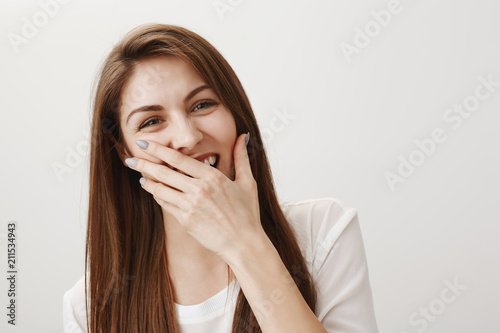 Girl want have some fun. Indoor shot of good-looking brunetter in white shirt laughing out loud, covering opened mouth with hand, hearing emberrasing joke or attending stand-up show