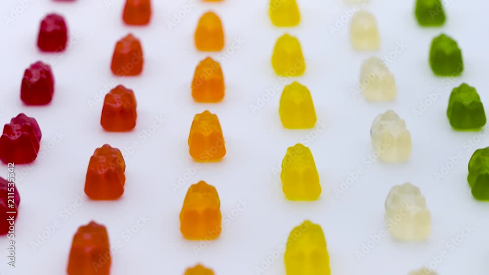 Colorful gummy bears, sweet fruit jelly candies rows are moving vertically on the white background Colorful gummy bears, sweet fruit jelly candies rows are moving vertically on the white background
