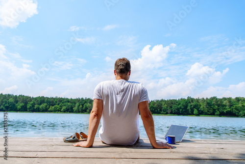man sitting with laptop and looking on lake. working at vacation. summer time concept photo