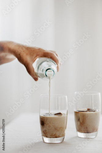 Frozen coffee ice cubes in a glass poured with milk to make a refreshing summer iced coffee drink. White background. Body parts.