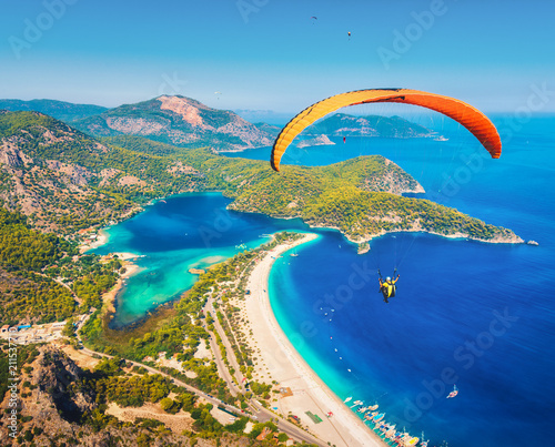 Fototapeta Naklejka Na Ścianę i Meble -  Paragliding in the sky. Paraglider tandem flying over the sea with blue water and mountains in bright sunny day. Aerial view of paraglider and Blue Lagoon in Oludeniz, Turkey. Extreme sport. Landscape