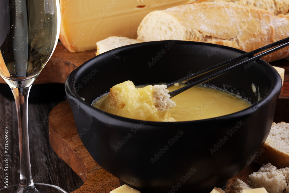 Gourmet Swiss fondue dinner on a winter evening with assorted cheeses on a board alongside a heated pot of cheese fondue with two forks dipping bread and white wine behind in a tavern or restaurant Gourmet Swiss fondue dinner on a winter evening with assorted cheeses on a board alongside a heated pot of cheese fondue with two forks dipping bread and white wine behind in a tavern or restaurant