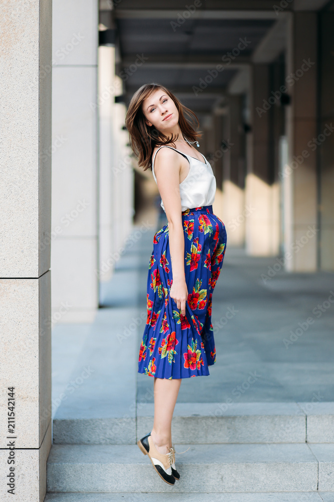 Woman jumping in the street. Woman portrait outdoors in floral skirt and white top. Fashion portrait of beautiful woman in the street, urban background.