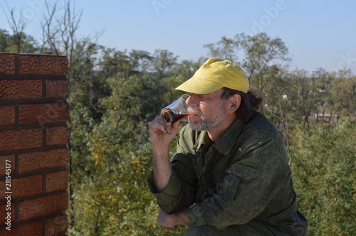 A construction worker interrupted his work and drinks coffee in the open air near the brickwork.