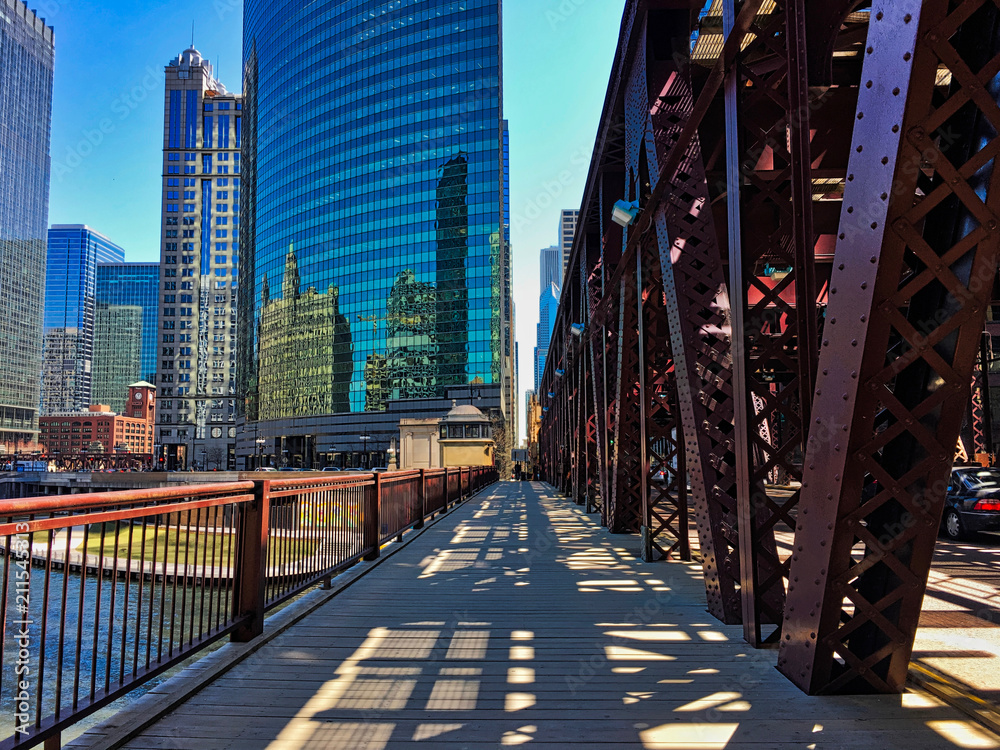 Chicago's elevated train tracks cast shadows on Lake Street and sidewalk along the river in downtown Loop. - obrazy, fototapety, plakaty 