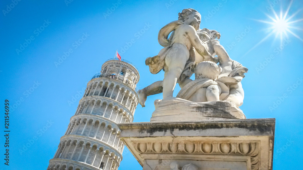 Leaning Tower of Pisa and statue of cherubs winged angels supporting heel of tower and shining fair bright sun with beams at clear blue sky, Pisa, Tuscany, Italy.