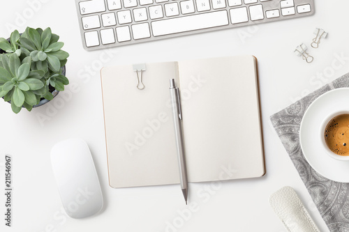 bright minimalist workspace / desktop with blank open notebook, office supplies, coffee and succulent plant on a white background - top view, copyspace photo