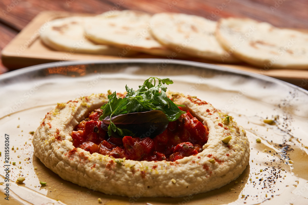 Hummus National Israeli cuisine. Hummus with harissa sauce and pistachios, close-up. Vegetarian diet food with pita bread on wooden cutting board. Hummus National Israeli cuisine. Hummus with harissa sauce and pistachios, close-up. Vegetarian diet food with pita bread on wooden cutting board.