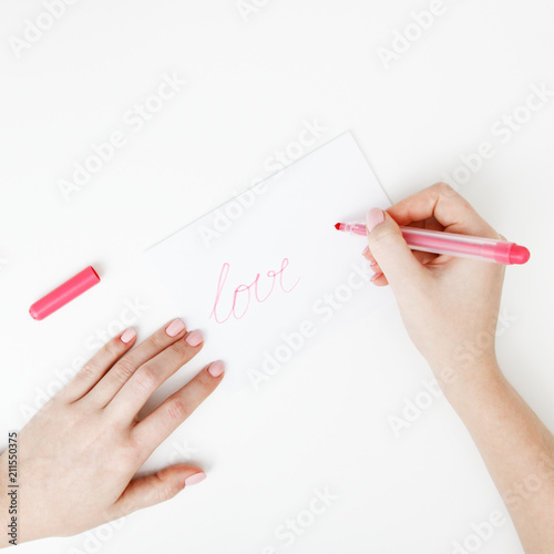 Flat lay. Top view. Hand of girl writing love letter on Saint Valentines Day. Handmade postcard with red heart shaped figure. Woman write Love on postcard for 14 February holiday celebration