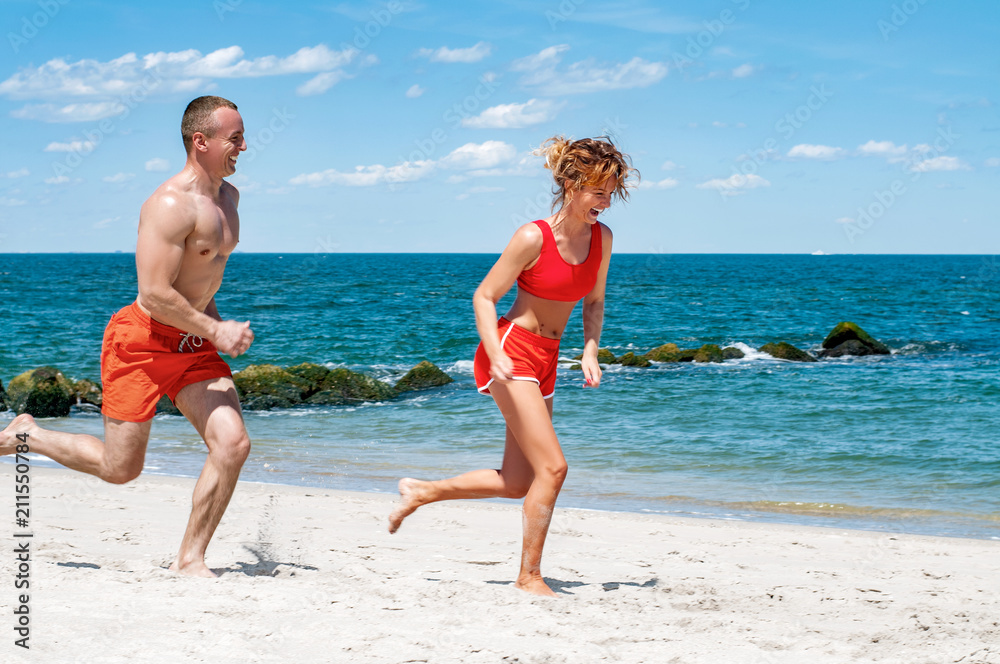 Happy couple running on beach. Man and woman jogging on the sea shore.