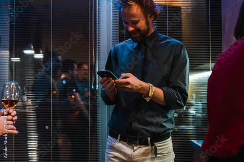Attractive man with curly hairstyle writing message on smartphone at the beautiful home