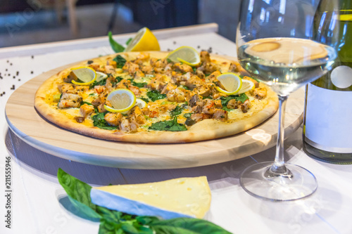 appetizing pizza with shrimps, lemon and a glass of wine on a white table